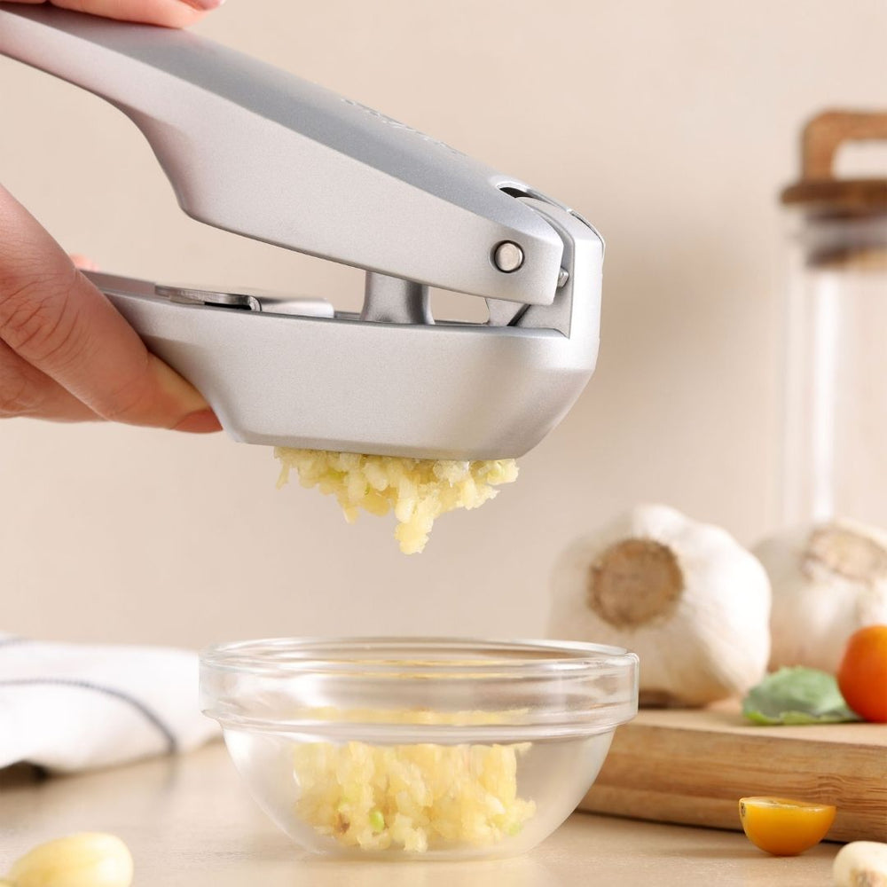 The Zyliss Susi 4 Garlic Press, featuring ergonomic handles and a sleek silver design, is shown closed on a plain light background, offering easy cleanup.