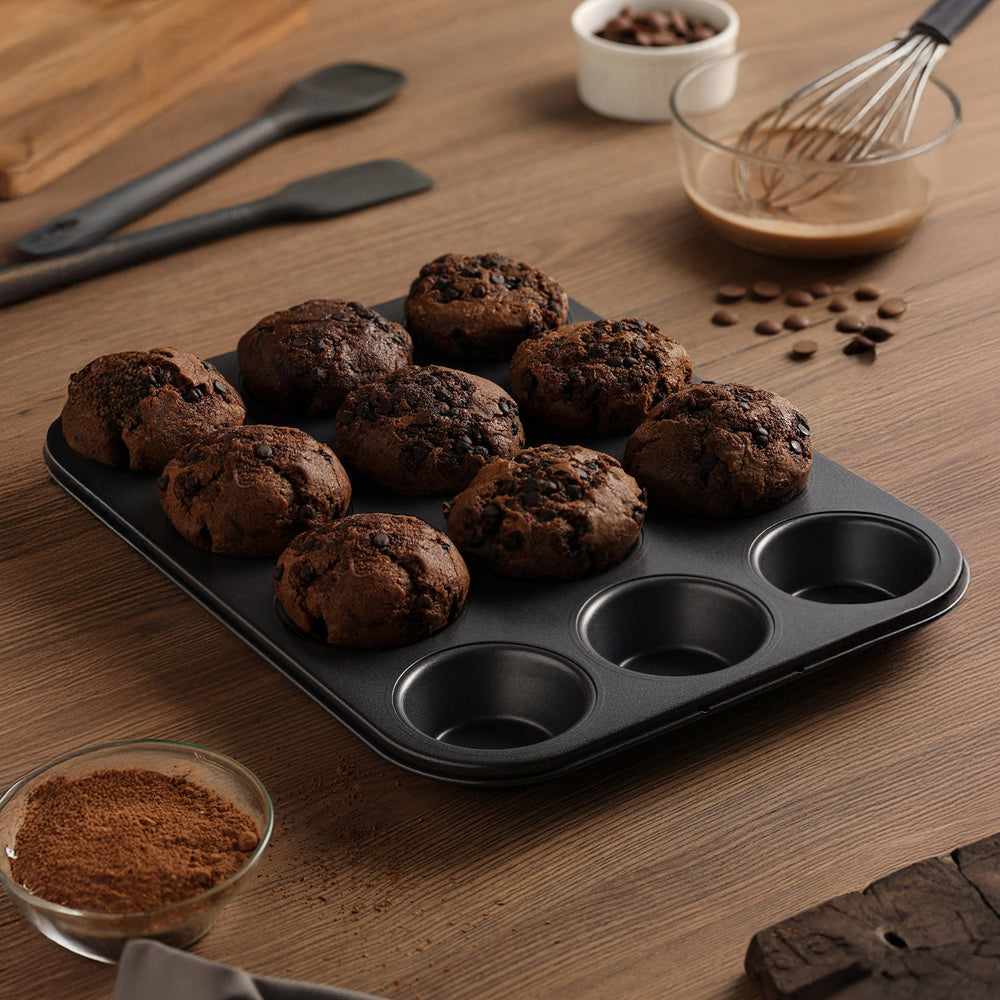 The Zyliss Non-Stick 12 Hole Muffin Pan, made from durable carbon steel and ideal for baking muffins or cupcakes, is displayed on a plain light background.
