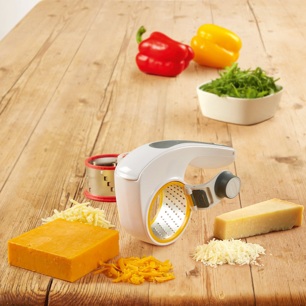 The Zyliss All Cheese Grater features stainless steel blades, interchangeable drums, a white handheld design, black grip, red drum rim, and gray push button for easy grating. 