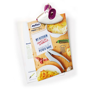 A Zyliss Clip-All Bag Clip (purple and white), a kitchen must-have, secures a garlic & potato bake recipe page with photos of baked dishes, garlic cloves, a peeler, and the line: My kitchen cant do without... GARLIC & POTATO BAKE. 