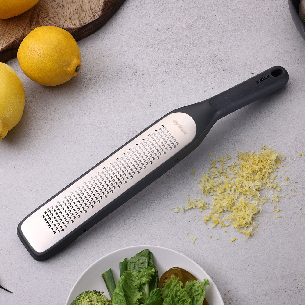 #belugagrey The Zyliss Rasp Grater is a long, rectangular foot file with a gray handle and textured metal surface for removing calluses and dead skin. The handle features a hanging hole for easy storage. 