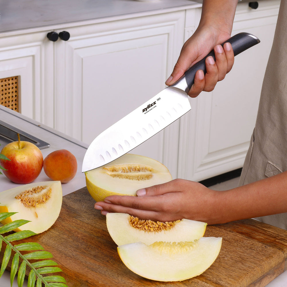 The Zyliss Comfort Pro Santoku Knife 18.5cm/7" features German stainless steel, an ergonomic gray handle, and oval blade indentations, shown on a plain light background.