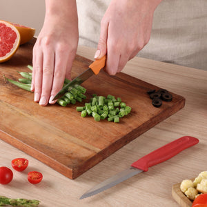 Someone chops green beans on a wooden cutting board using the Zyliss Classic 2 Piece Paring Knife Set. Sliced green beans, black olives, half a grapefruit, another knife with ergonomic handles, and various vegetables are nearby.