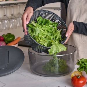 Using the Zyliss Swift Dry Salad Spinner’s one-handed pump, a person dries lettuce, then transfers crisp leaves into a salad bowl on the kitchen counter amid fresh vegetables and the spinner lid.