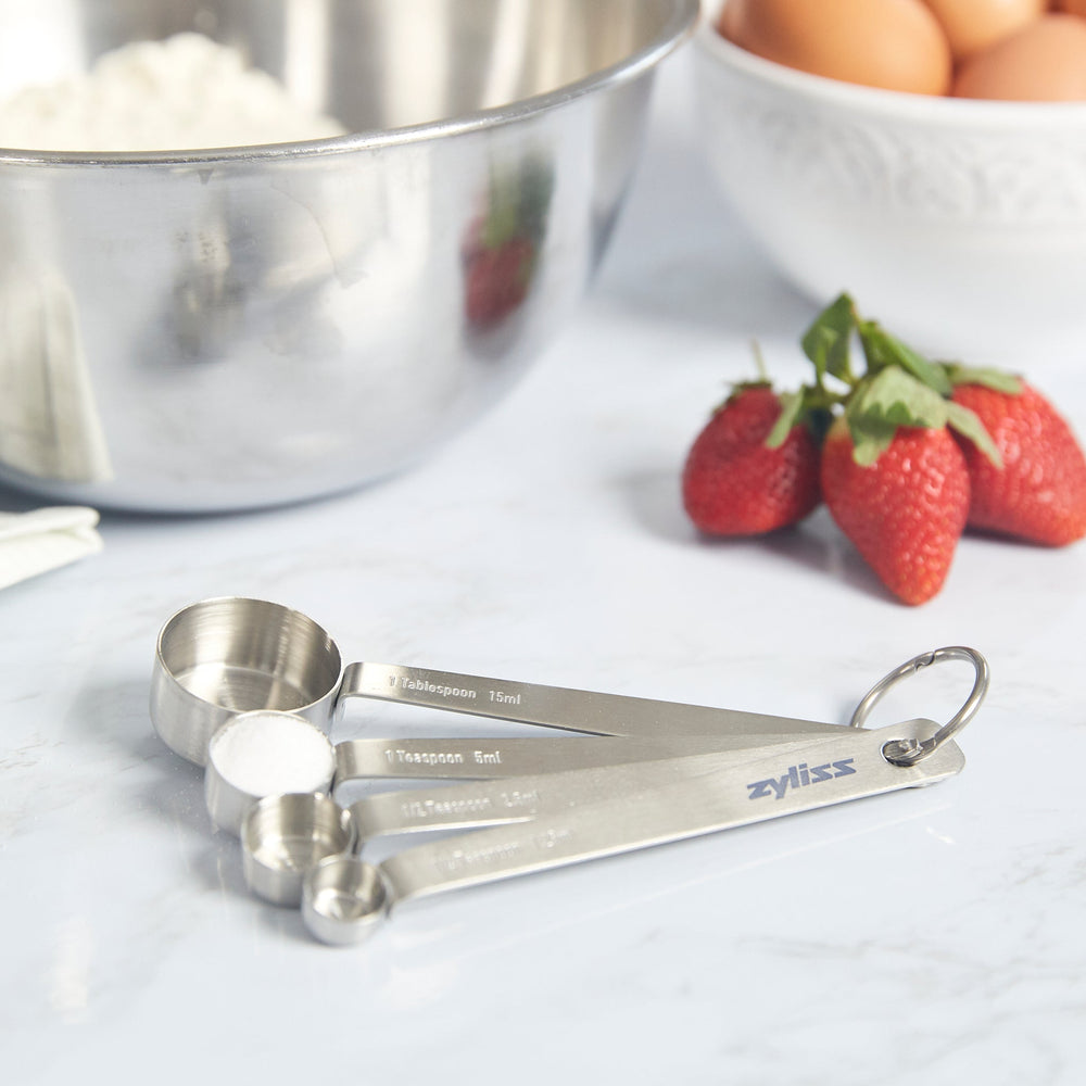 The Zyliss Stainless Steel Measuring Spoons set includes four essential kitchen tools, connected by a metal ring and shown on a plain light background. 