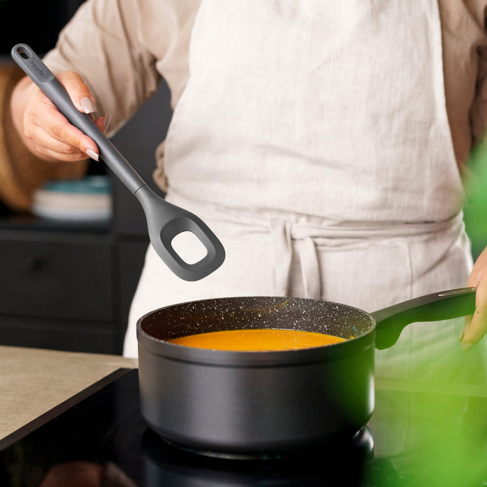 The Zyliss Square Mixing Spoon is a gray, heat-resistant silicone utensil with a long handle and a rectangular hole in the head. Shown on a plain light background, its dishwasher safe for easy cleaning. 