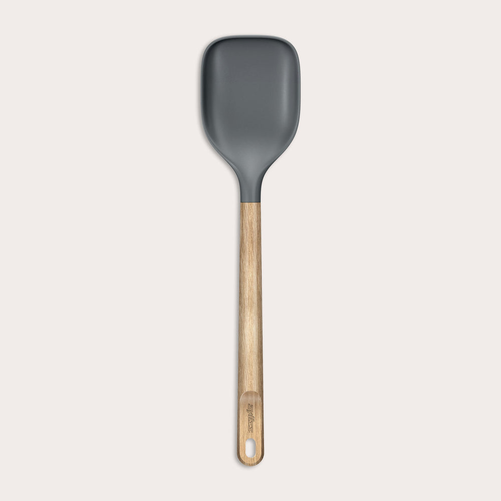 The Zyliss Oak Wood Spoon Large features a gray silicone head, an oak wood handle with a hanging hole, and is shown on a plain white background—a versatile utensil for home cooks.