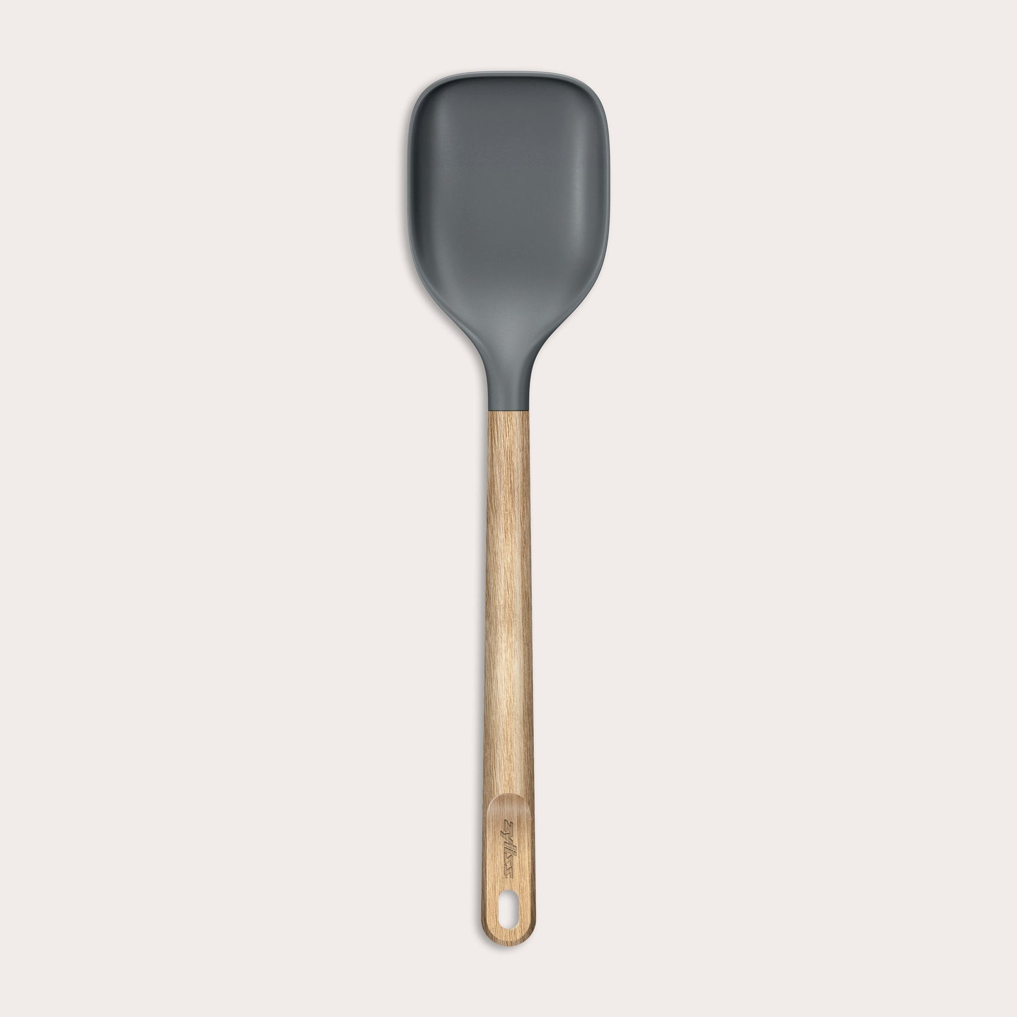 The Zyliss Oak Wood Spoon Large features a gray silicone head, an oak wood handle with a hanging hole, and is shown on a plain white background—a versatile utensil for home cooks.