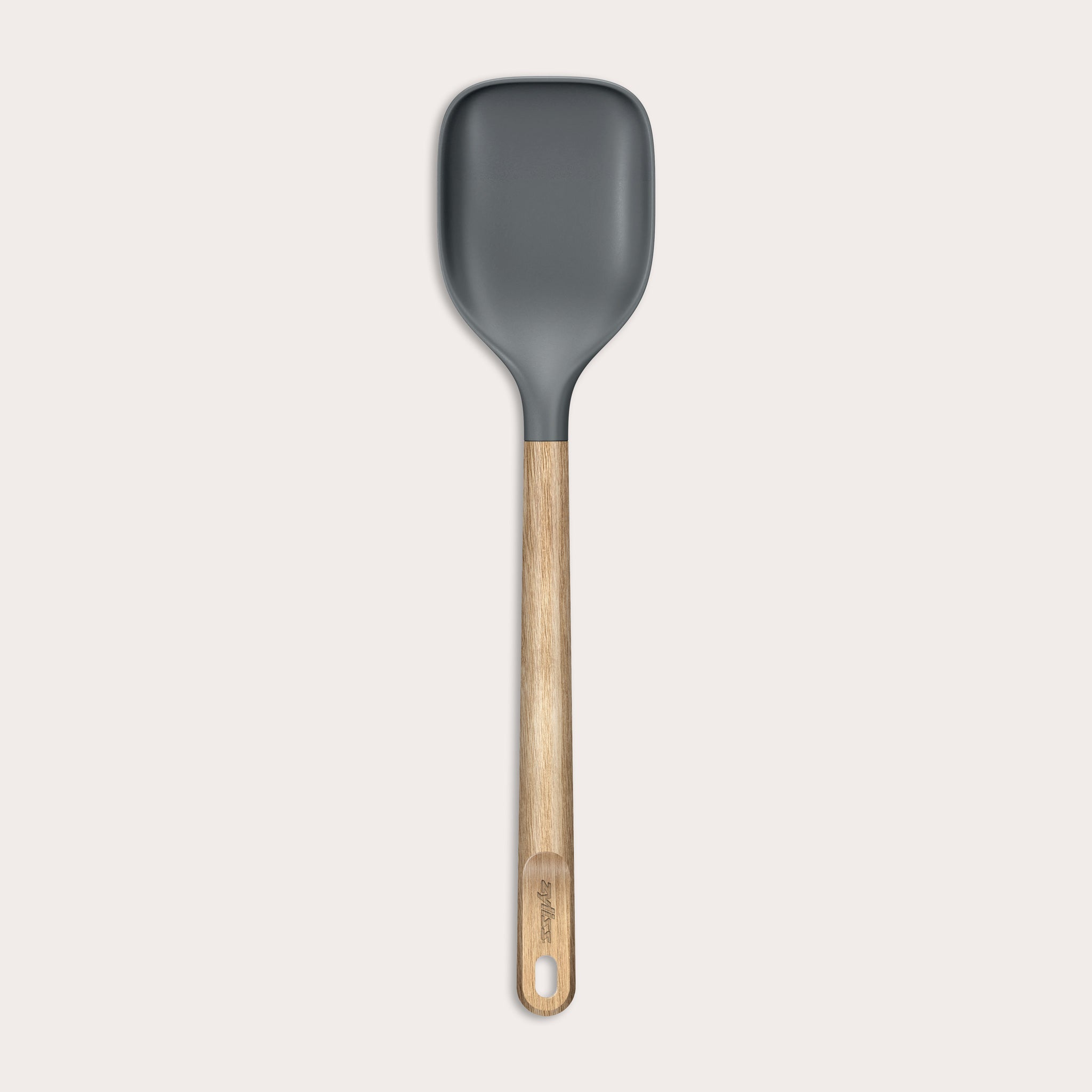 The Zyliss Oak Wood Spoon Large features a gray silicone head, an oak wood handle with a hanging hole, and is shown on a plain white background—a versatile utensil for home cooks.