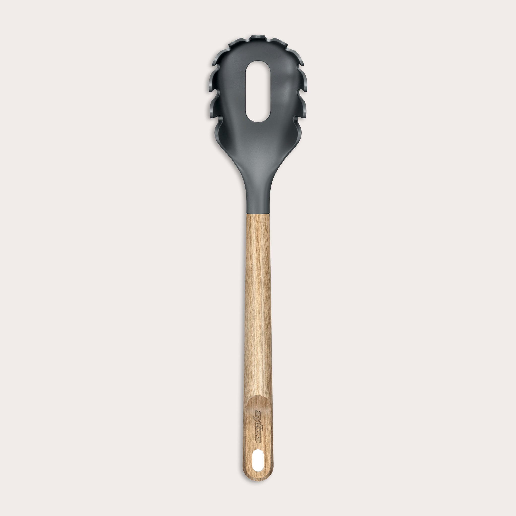 The Zyliss Oak Wood Spaghetti Server is a black utensil with an oak handle, pronged edges, and a large oval center hole, shown on a plain light background.