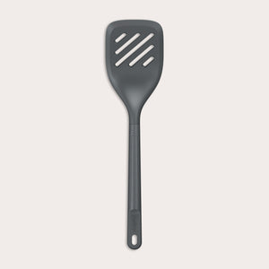 The Zyliss Slotted Turner, shown in black with three diagonal slots and an ergonomic handle, features a heat-resistant design for safe cooking or flipping food. Displayed against a plain white background. 