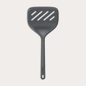 A Zyliss Turner XL slotted spatula in black, featuring a wide square head with three diagonal slots, ergonomic handle, and heat-resistant design is displayed against a plain light background. 