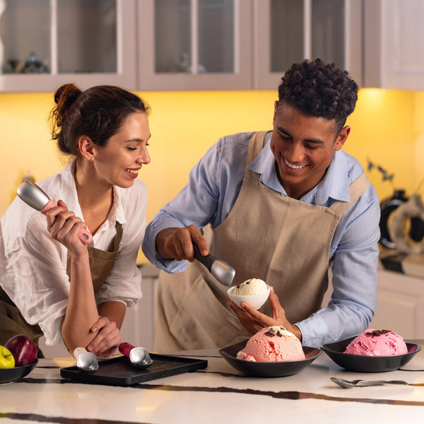 #pink Two people in a kitchen smile as they use the Zyliss Ice Cream Scoop to serve white, pink, and light brown ice cream into bowls. Three large bowls of ice cream sit on the counter.
