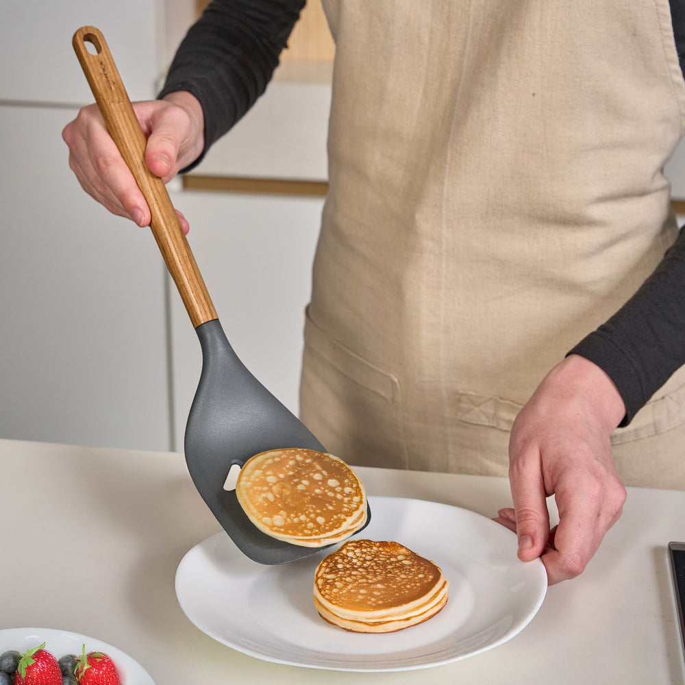 The Zyliss Oak Wood Slotted Turner is a kitchen essential with a wide, dark gray head and light oak wood handle, shown on a plain white background.