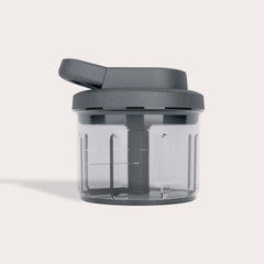 The Zyliss Easy Pull Food Processor is a compact chopper with a transparent body, dark gray lid and handle, internal blades, and a minimalist design, shown against a light background.