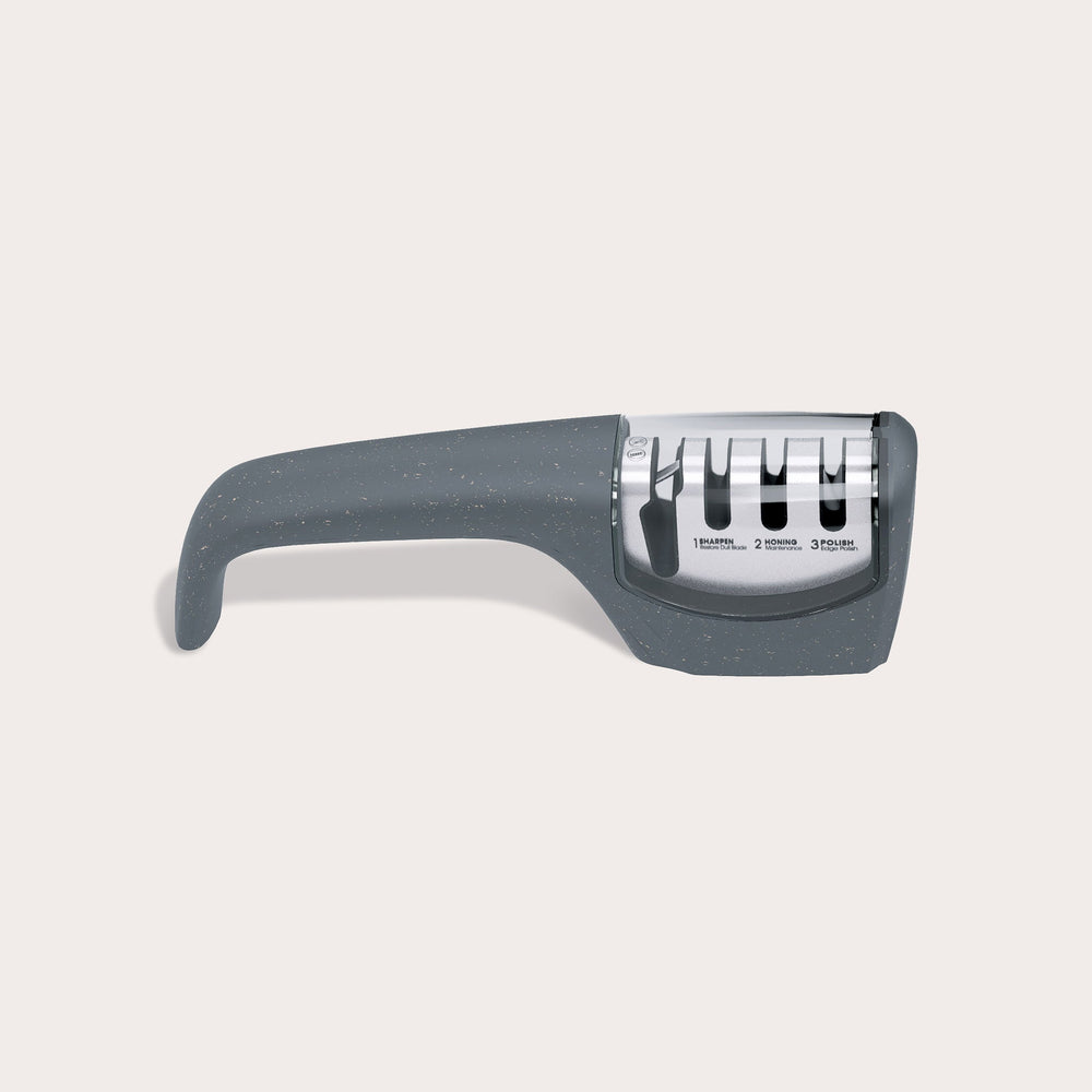 The Zyliss Knife Sharpener features a gray ergonomic handle and three sharpening slots for kitchen blades and serrated edges, displayed on a plain, light background.