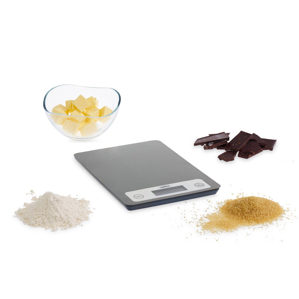 The Zyliss Electronic Measuring Scale sits on a white background, surrounded by a glass bowl of cubed butter, chocolate pieces, flour, and brown sugar—ideal for precise baking measurements. 