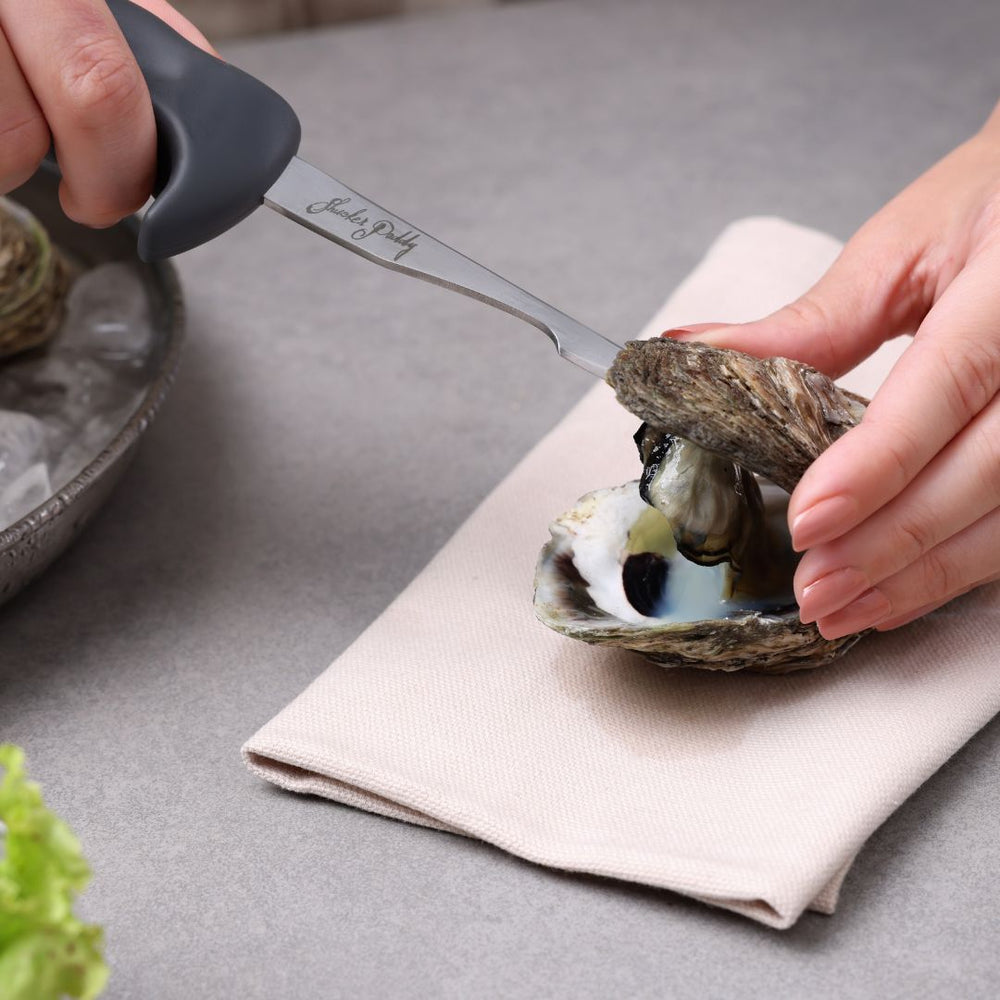 The Zyliss Oyster Knife Shucker Paddy features a metal hook blade, curved ergonomic black handle, and engraved signature—ideal for precise oyster shucking. Shown against a plain white background.