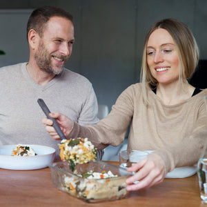 #0.64L/0.67qt A smiling woman serves food from a Zyliss 2-Piece Glass Container Set at the table, while a man beside her looks on with a smile. Both appear relaxed and are enjoying their meal together.