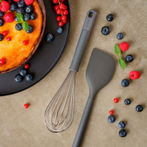 A cheesecake topped with blueberries, red currants, and mint sits beside a Zyliss Balloon Whisk and a gray spatula on the countertop, surrounded by berries—ideal tools for non-stick cookware. #Large